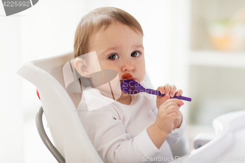 Image of baby with spoon eating food at home