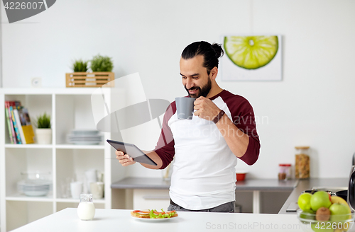 Image of man with tablet pc eating at home kitchen