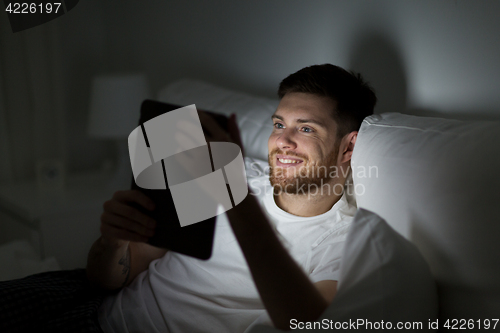 Image of young man with tablet pc in bed at home bedroom