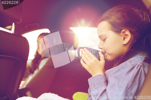 Image of little girl driving in car and drinking from cup