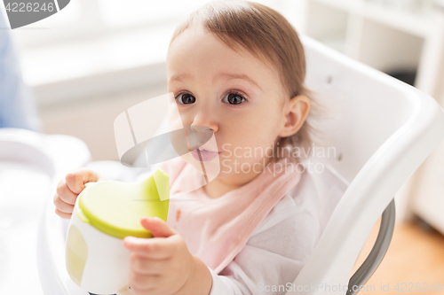 Image of baby drinking from spout cup in highchair at home