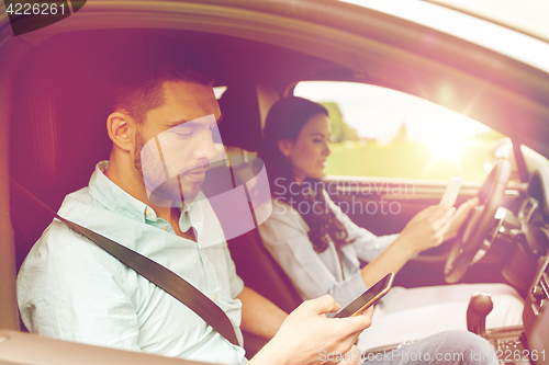 Image of man and woman with smartphones driving in car
