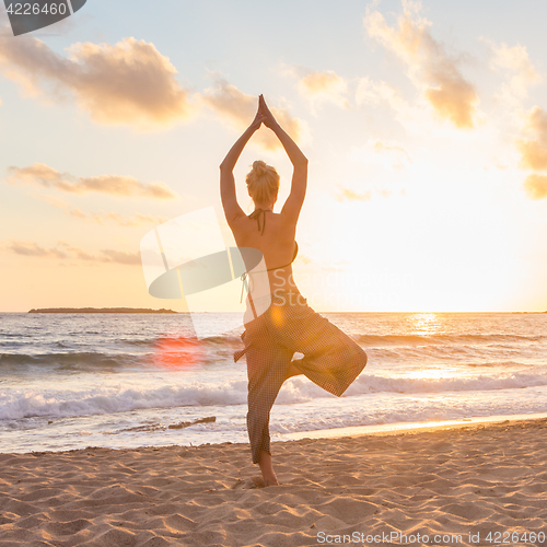 Image of Woman practicing yoga on sea beach at sunset.