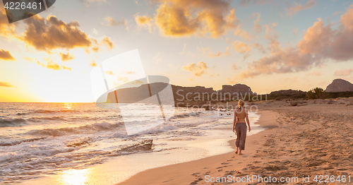 Image of Woman walking on sandy beach at sunset.