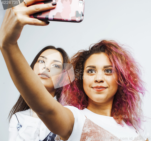 Image of lifestyle people concept: two pretty stylish modern hipster teen girl having fun together, diverse nation mixed races, happy smiling making selfie 