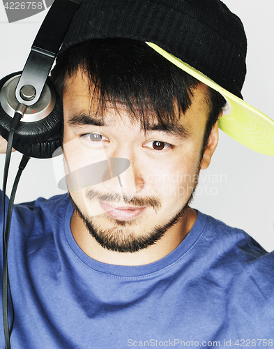 Image of young asian man in hat and headphones listening music on white b