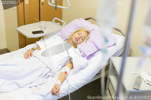 Image of Bedridden female patient recovering after surgery in hospital care.