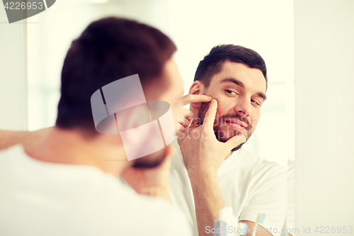 Image of man squeezing pimple at bathroom mirror