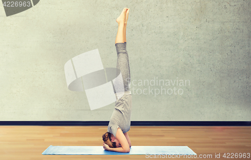 Image of woman making yoga in headstand pose on mat
