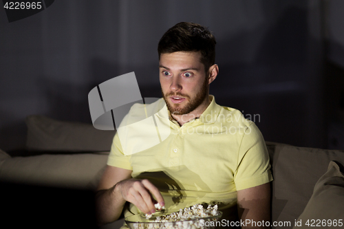 Image of man watching tv and eating popcorn at night