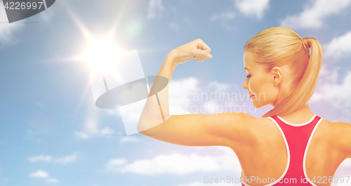 Image of happy sporty woman showing biceps over sky and sun