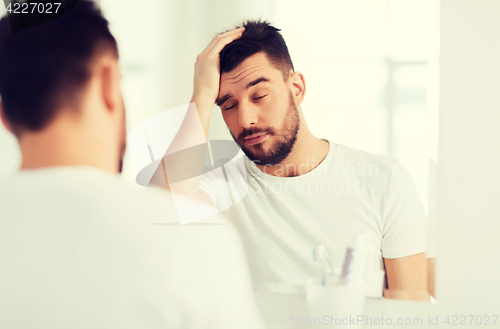 Image of sleepy young man in front of mirror at bathroom