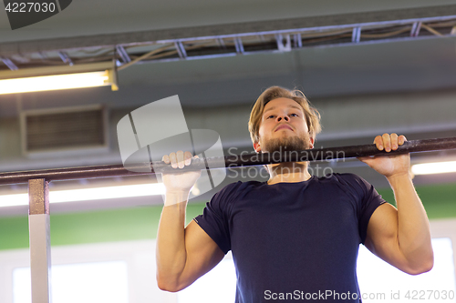 Image of man exercising on bar and doing pull-ups in gym