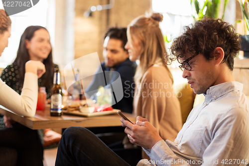 Image of man with smartphone and friends at restaurant