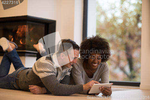 Image of multiethnic couple using tablet computer on the floor