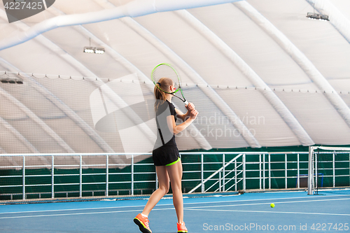 Image of The young girl in a closed tennis court with ball