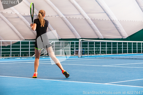 Image of The young girl in a closed tennis court with ball