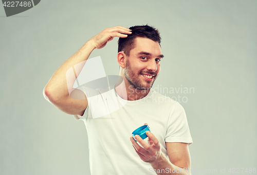 Image of happy young man styling his hair with wax or gel