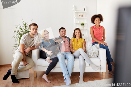 Image of happy friends with remote watching tv at home