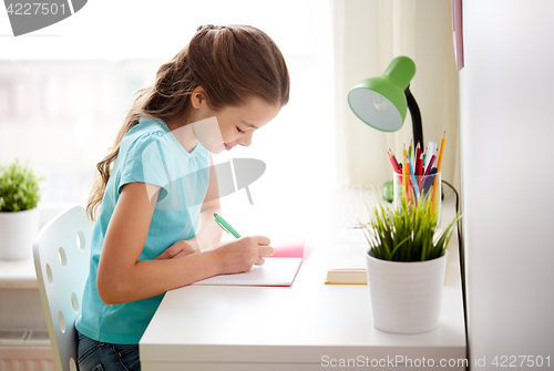 Image of happy girl writing to notebook at home