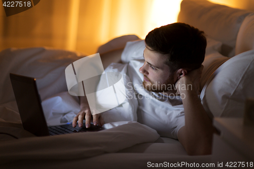 Image of young man with laptop in bed at home bedroom