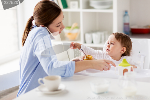 Image of mother with smartphone feeding baby at home
