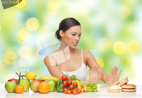 Image of woman with fruits rejecting fast food on table