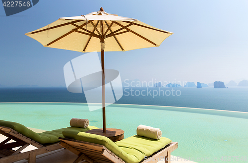 Image of infinity pool with parasol and sun beds at ocean