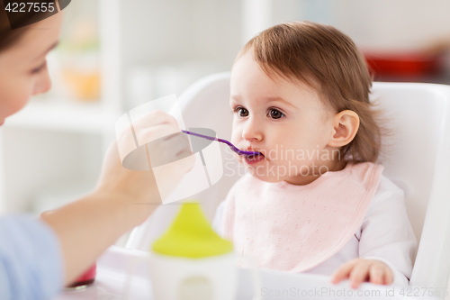 Image of happy mother feeding baby with puree at home