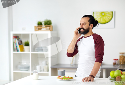 Image of man calling on smartphone and eating at home