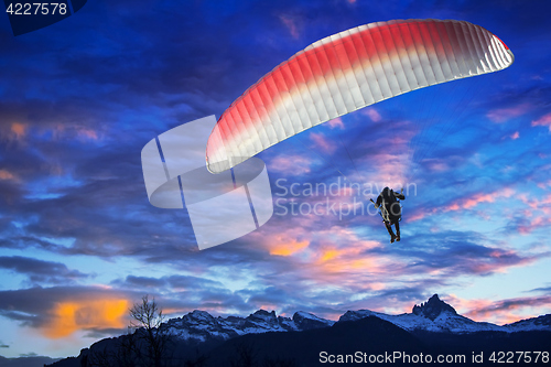 Image of Paraglider flying over mountains in winter sunset