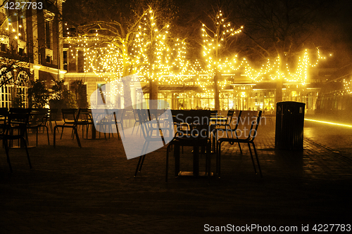 Image of empty night restaurant, lot of tables and chairs with noone, magic fairy lights on trees like christmas celebration