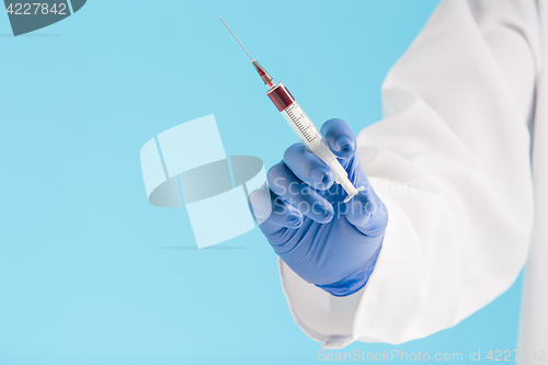 Image of Hand in a blue glove holding syringe on blue