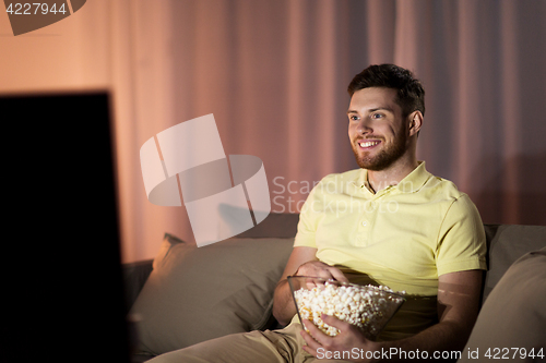 Image of happy man with popcorn watching tv at night