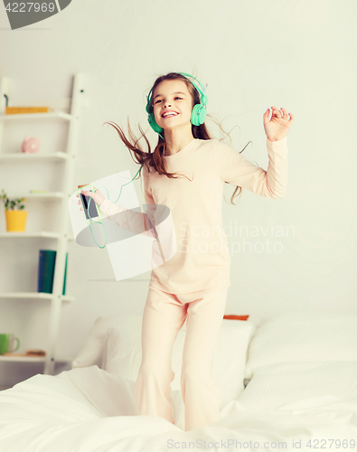 Image of girl jumping on bed with smartphone and headphones