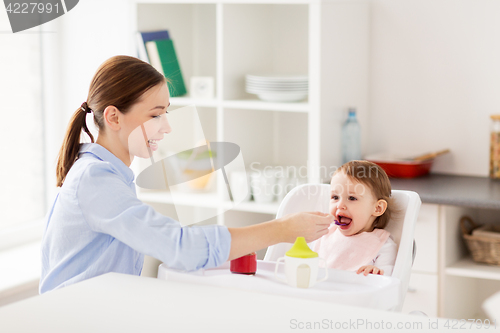 Image of happy mother feeding baby with puree at home