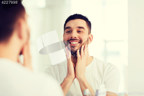 Image of happy young man looking to mirror at home bathroom