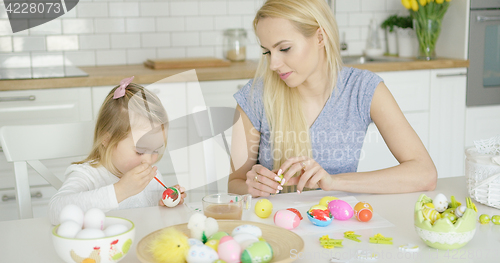 Image of Mother looking at girl coloring eggs