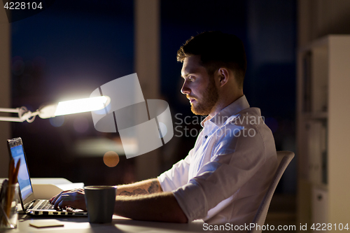 Image of man with laptop and coffee working at night office