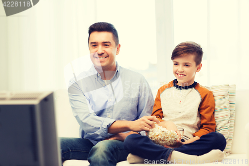 Image of smiling father and son watching tv at home