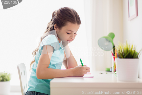 Image of happy girl writing to notebook at home