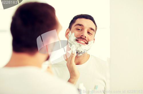 Image of happy man applying shaving foam at bathroom mirror