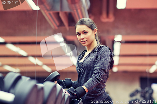 Image of young woman choosing dumbbells in gym