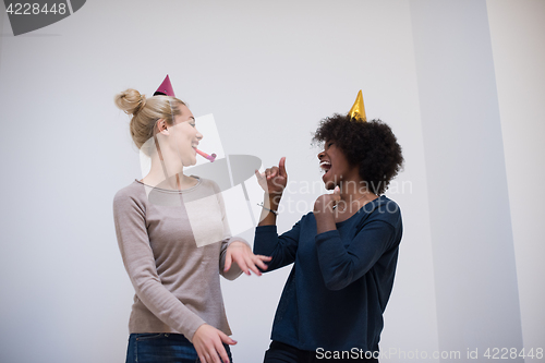 Image of smiling women in party caps blowing to whistles