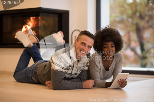 Image of multiethnic couple using tablet computer on the floor