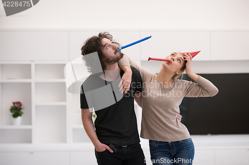 Image of couple in party hats blowing in whistle