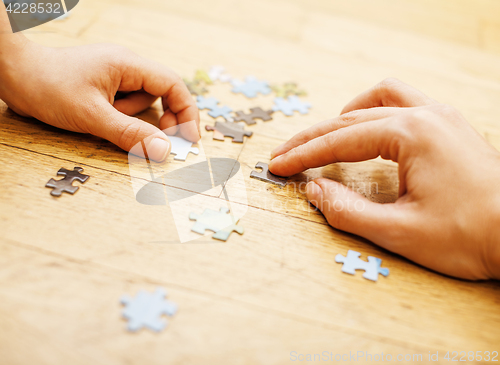 Image of little kid playing with puzzles on wooden floor together with parent, lifestyle people concept, loving hands to each other 