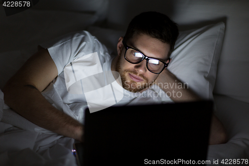 Image of young man with laptop in bed at home bedroom