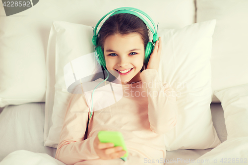 Image of happy girl lying in bed with smartphone at home