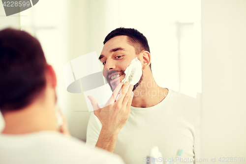 Image of happy man applying shaving foam at bathroom mirror